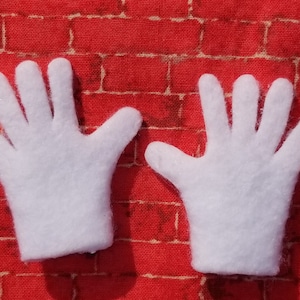 Könnte beinhalten: Zwei weiße Filzhandschuhe mit jeweils fünf Fingern. Die Handschuhe liegen auf einem roten Ziegelhintergrund.