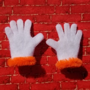 Könnte beinhalten: Ein Paar weiße Filzhandschuhe mit orangefarbenem Fellbesatz. Die Handschuhe liegen flach auf einem roten Ziegelhintergrund.
