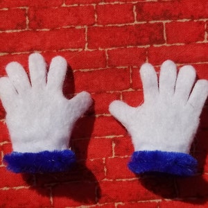 Könnte beinhalten: Ein Paar weiße Filzhandschuhe mit blauen, flauschigen Manschetten. Die Handschuhe liegen flach auf einem roten Ziegelhintergrund.