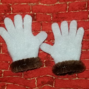 May include: A pair of white felt gloves with brown fur trim. The gloves are on a red brick background.