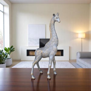 May include: A silver and gold giraffe statue with a textured surface. The giraffe is standing on a wooden table.