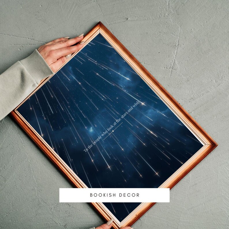 May include: A framed print with a dark blue background and white shooting stars. The print has the text "To the people who look at the stars and wish" in white text. The frame is gold and the print has the text "BOOKISH DECOR" in white text at the bottom.
