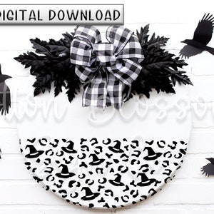 May include: A white round door hanger with a black and white checkered bow and black leaves. The bottom half of the door hanger is decorated with a black and white pattern of witch hats and leopard spots. There are five black crow silhouettes around the door hanger.