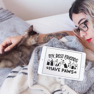 May include: A white tablet with a black screen displaying the text "My best friends have paws" with a graphic of paw prints and hearts. The tablet is lying on a grey and white blanket.