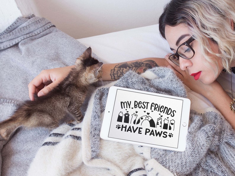 May include: A white tablet with a black screen displaying the text "My best friends have paws" with a graphic of paw prints and hearts. The tablet is lying on a grey and white blanket.