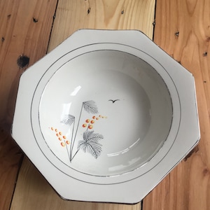 May include: White octagonal ceramic bowl with a silver rim and a floral design in black and orange. The bowl has a small bird design in the centre.