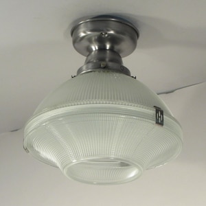 May include: A vintage ceiling light fixture with a clear, ribbed glass shade and a brushed metal base. The shade has a rounded, bowl-like shape and is secured with a metal clip. The fixture is mounted on a white ceiling.
