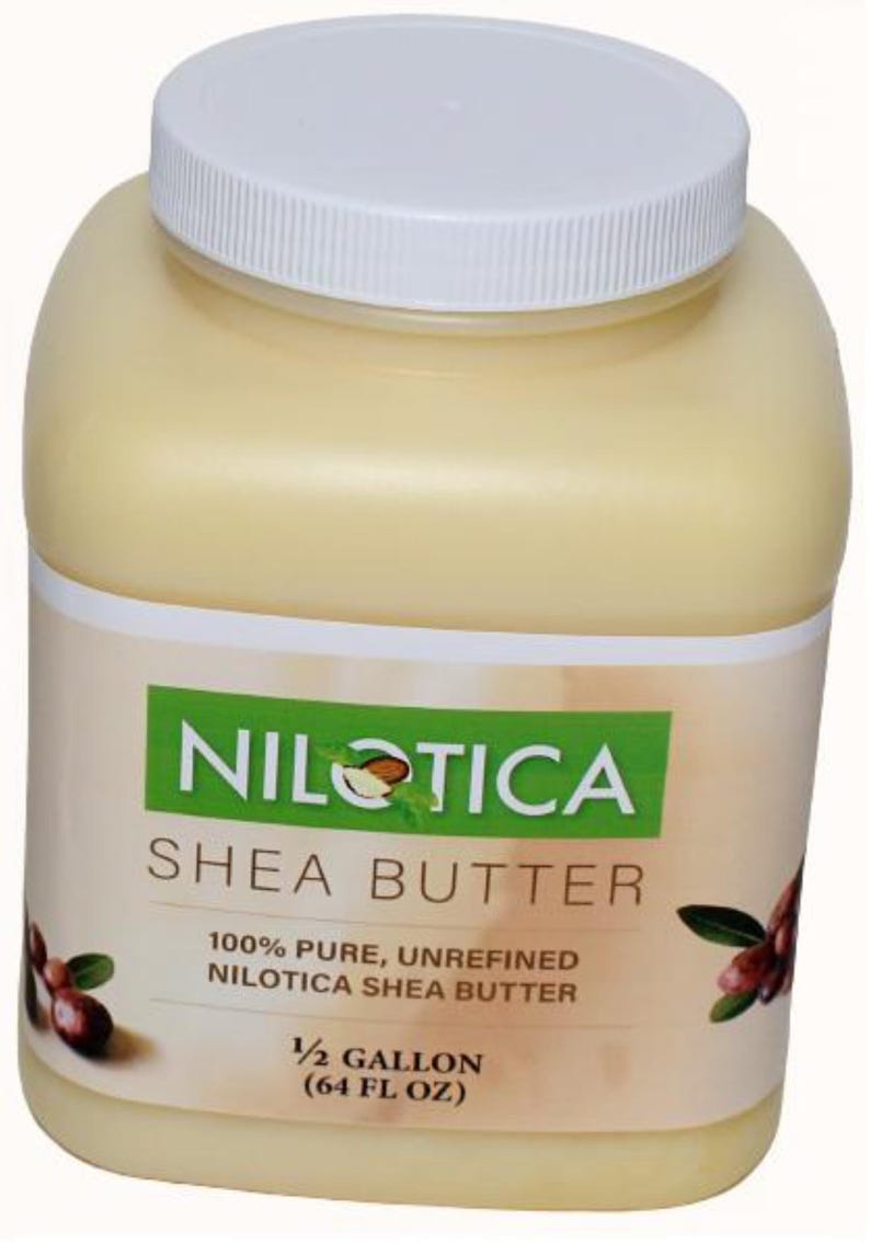 May include: A large, off-white plastic jar with a white lid. The label reads "NILOTICA SHEA BUTTER" and "100% PURE, UNREFINED NILOTICA SHEA BUTTER". The jar contains a light yellow substance, and is labeled as 1/2 gallon (64 fl oz).