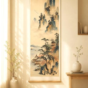May include: A vertical wall hanging scroll featuring a watercolor landscape painting. The artwork depicts towering blue and brown mountains shrouded in mist, pine trees, traditional buildings near a calm body of water, and small birds in flight.