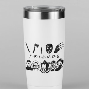 以下が含まれることがあります： 黒いホラー映画のキャラクターのグラフィックと「FRIENDS」というテキストが書かれた白いステンレス製のタンブラー。テキストの上に黒い斧、ホッケーマスク、爪痕があります。