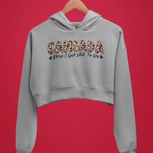 May include: A gray cropped hoodie with a leopard print design that says "Cansada pero I got shit to do" in black text.