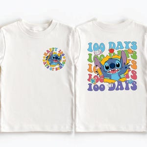 two white t-shirts with colorful designs and text. The t-shirt on the left has a small circular design with a cartoon character, and the t-shirt on the right has a larger design with a cartoon character and text that reads "100 DAYS 100 DAYS 100 DAYS".