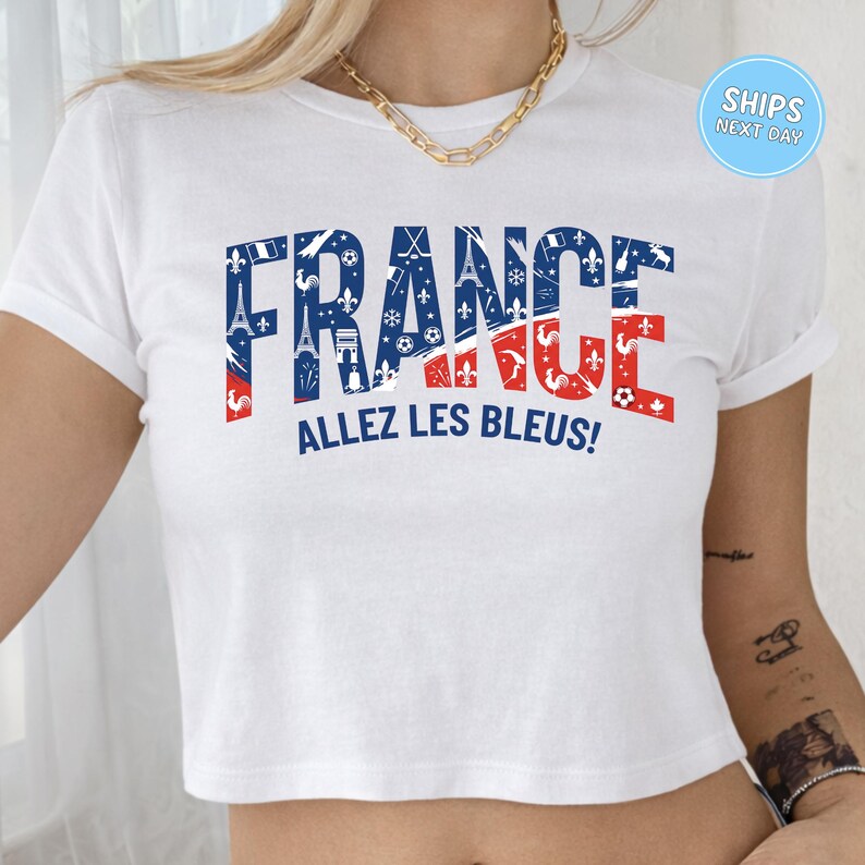 A white crop top with the word "FRANCE" printed on it in a stylized design, along with the phrase "ALLEZ LES BLUES!" printed below.