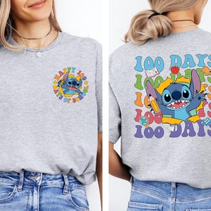 A woman wearing a gray t-shirt with a colorful graphic design featuring a cartoon character and the text "100 DAYS 100 DAYS 100 DAYS".
