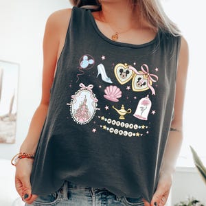 A woman wearing a black tank top with a graphic design featuring various Disney-themed elements such as Mickey Mouse, Minnie Mouse, a castle, and a magic lamp.