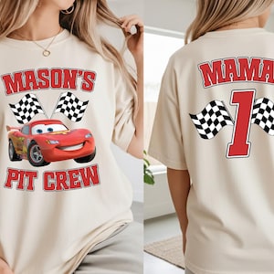 A woman wearing a white t-shirt with a red and black design featuring a red car and checkered flags, along with the text "Mason's Pit Crew" and the number "1".