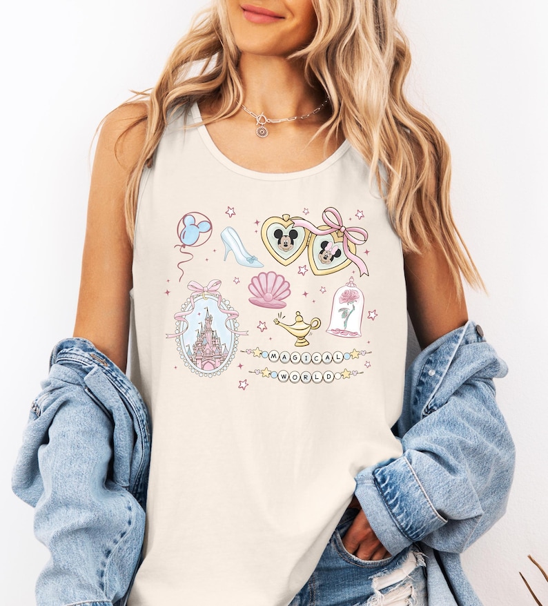 A woman wearing a white tank top with a Disney-themed design, including a castle, Mickey Mouse, and other whimsical elements. She is also wearing a denim jacket and has her hands in her pockets.