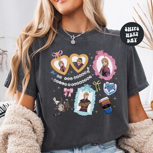 A woman wearing a gray t-shirt with various cartoon-style illustrations and text, including characters and objects such as hearts, bows, and a cup.