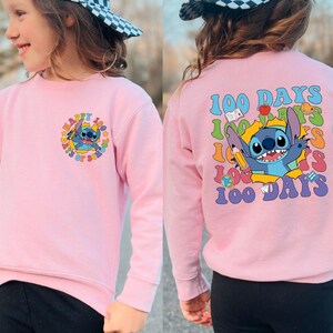 A young girl wearing a pink sweatshirt with a cartoon character and text printed on it.