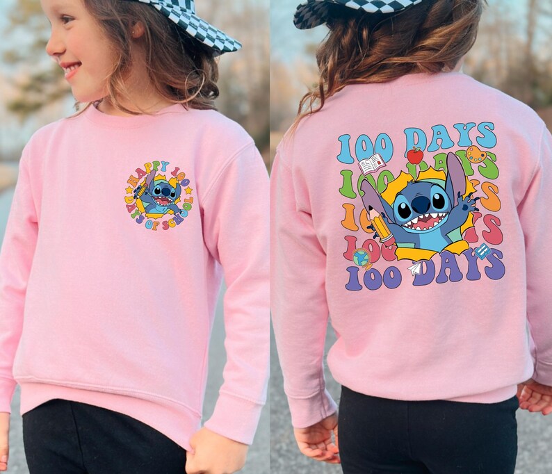 A young girl wearing a pink sweatshirt with a cartoon character and text printed on it.
