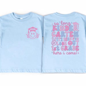 A light blue t-shirt with a pink graduation cap and a message about a first-grade teacher.