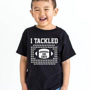 A young boy wearing a black t-shirt with a graphic design and text printed on it.
