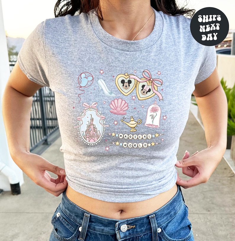 A woman wearing a gray t-shirt with a graphic design featuring various Disney-themed elements such as Mickey Mouse, a castle, and a rose.