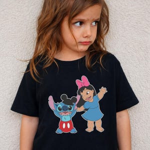 A young girl wearing a black t-shirt with a graphic of two cartoon characters, Stitch and Mickey Mouse, standing next to each other.