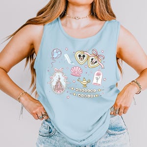 A woman wearing a light blue tank top with various Disney-themed illustrations and accessories, including a castle, Mickey Mouse, and other whimsical elements.