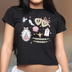 A woman wearing a black t-shirt with various Disney-themed illustrations and text, including a castle, Mickey Mouse, and other whimsical elements.