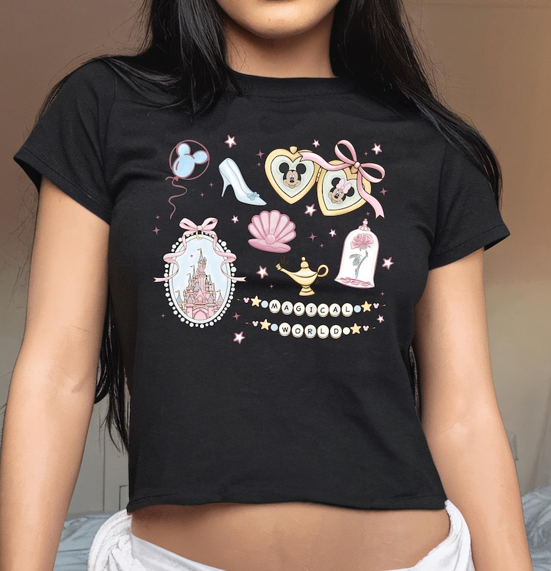 A woman wearing a black t-shirt with various Disney-themed illustrations and text, including a castle, Mickey Mouse, and other whimsical elements.