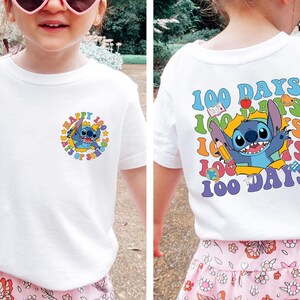 A young girl wearing a white t-shirt with a colorful graphic design featuring a cartoon character and text.