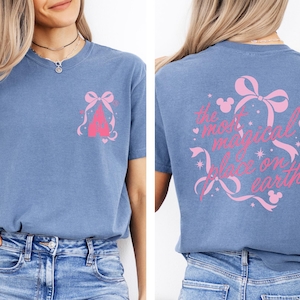 A woman wearing a blue t-shirt with a Disney castle graphic and text on the back.