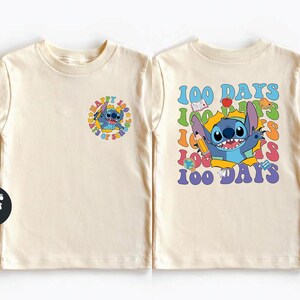 two white t-shirts with colorful designs and text. The t-shirt on the left has a small circular design with a cartoon character, while the t-shirt on the right has a larger design with a cartoon character and the text "100 DAYS" written around it.
