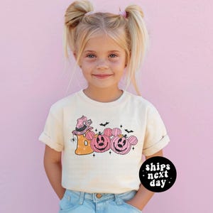 a little girl wearing a t - shirt with pumpkins that says boo