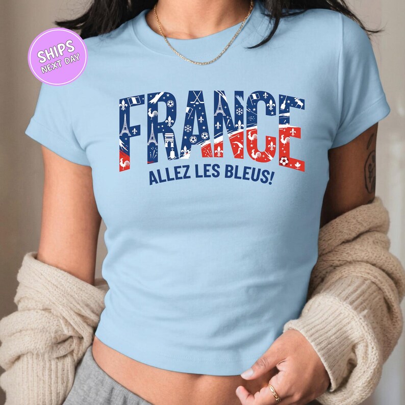 A woman wearing a light blue t-shirt with the text "FRANCE ALLEZ LES BLUES!" printed on it.
