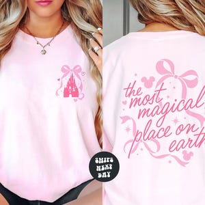 A woman wearing a pink t-shirt with a Disney castle design and the text "the most magical place on earth" printed on the back.