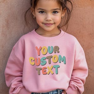 a little girl wearing a pink sweatshirt with a custom text on it