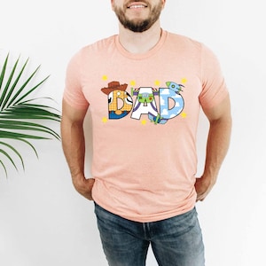 a man standing in front of a plant wearing a pink shirt with the word dad