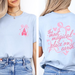 A woman wearing a light blue t-shirt with a pink castle graphic and the text "the most magical place on earth" printed on the back.