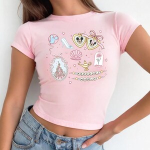 A woman wearing a pink crop top with various Disney-themed illustrations, including Mickey Mouse, a castle, and other whimsical objects.