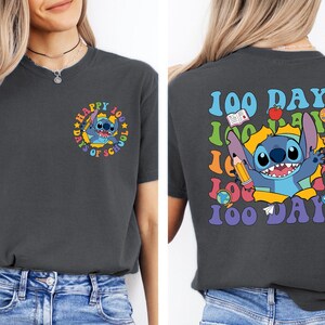 a woman wearing a black t-shirt with a colorful graphic design on the back. The design includes a cartoon character and text related to the 100 Days of School.