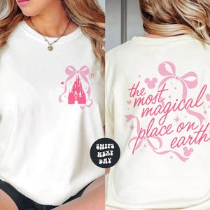 A woman wearing a white t-shirt with a pink castle and hearts printed on it. The t-shirt has text on the back that says "the most magical place on earth".