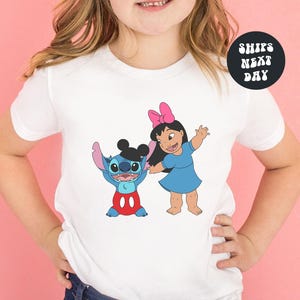 A young girl wearing a white t-shirt with a graphic of Stitch and Lilo from the Disney movie Lilo & Stitch.