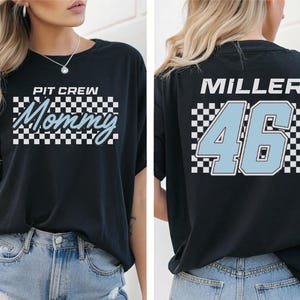 A woman wearing a black t-shirt with a checkered pattern and the text "PIT CIRCLE MOMMY 46" printed on it.