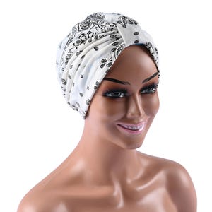 Peut inclure: Un turban blanc avec un motif paisley noir. Le turban est porté sur un mannequin à la peau brune.