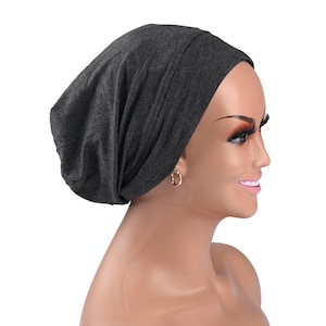 May include: A dark gray beanie-style hat made of soft fabric. The hat is shown on a mannequin head with gold hoop earrings. The hat is designed to cover the head and ears.