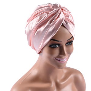 May include: A pink satin turban style hair wrap. The wrap is tied in a knot on top of the head.
