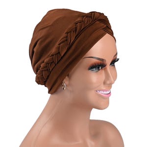 May include: A brown turban with a braided detail. The head covering is made of a soft fabric. The braided detail adds a decorative element to the turban. The turban is designed to be worn on the head.
