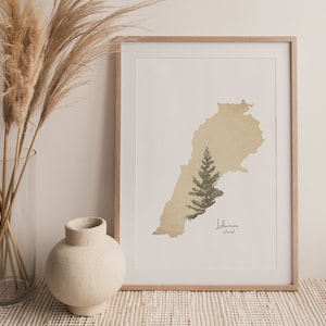 May include: A framed print of a map of Lebanon with a green tree in the center. The map is beige and the text "Lebanon" is written in English and Arabic below the tree.